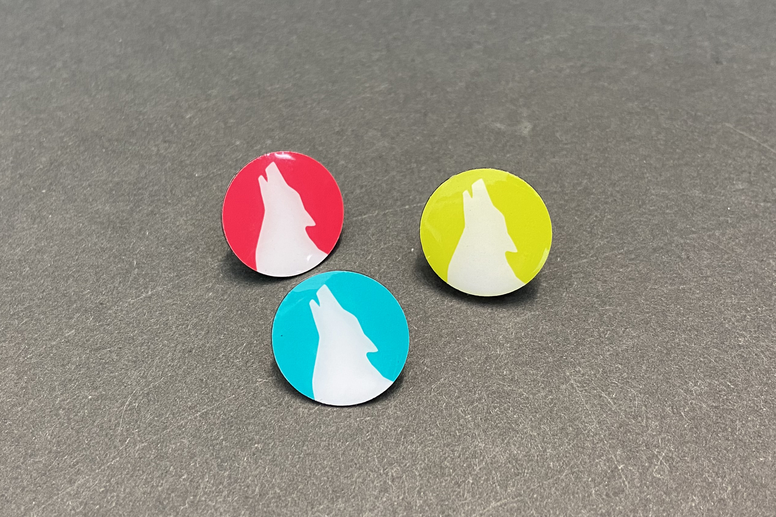 Das Bild zeigt ein 3er-Set Ansteckpins mit dem Wolfskopf in den drei Farben Candy, Petrol und Lemon.