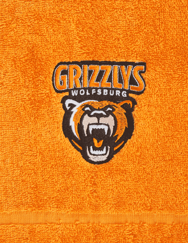 Das Foto zeigt ein Handtuch der Grizzlys Wolfsburg in orange mit aufgesticktem Logo.